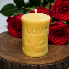 Load image into Gallery viewer, Beeswax candle with 'Love' embossed on it, surrounded by red roses on a wooden surface.